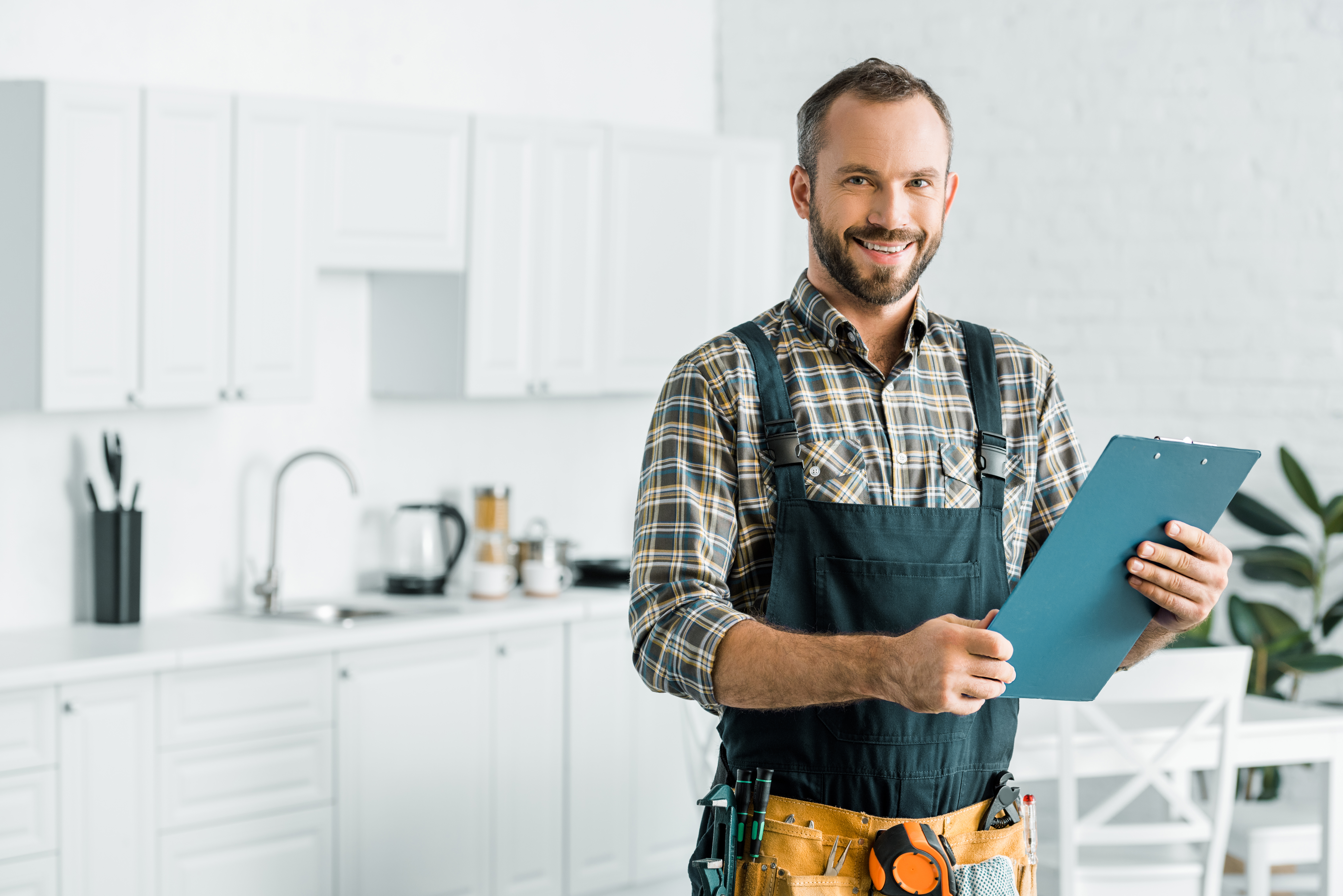 Homme souriant en salopette tient une planchette.