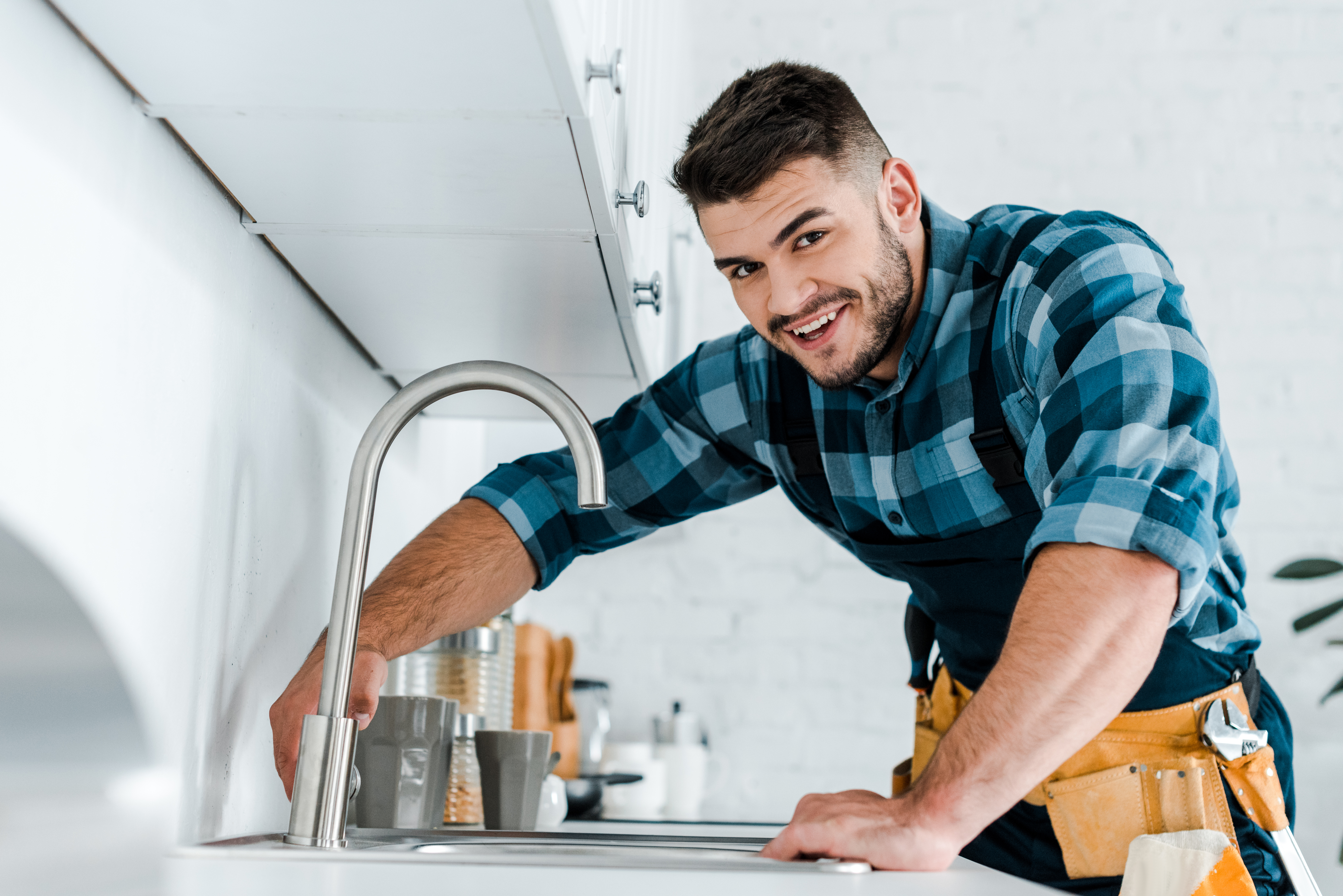 Plombier souriant travaillant au robinet de cuisine.