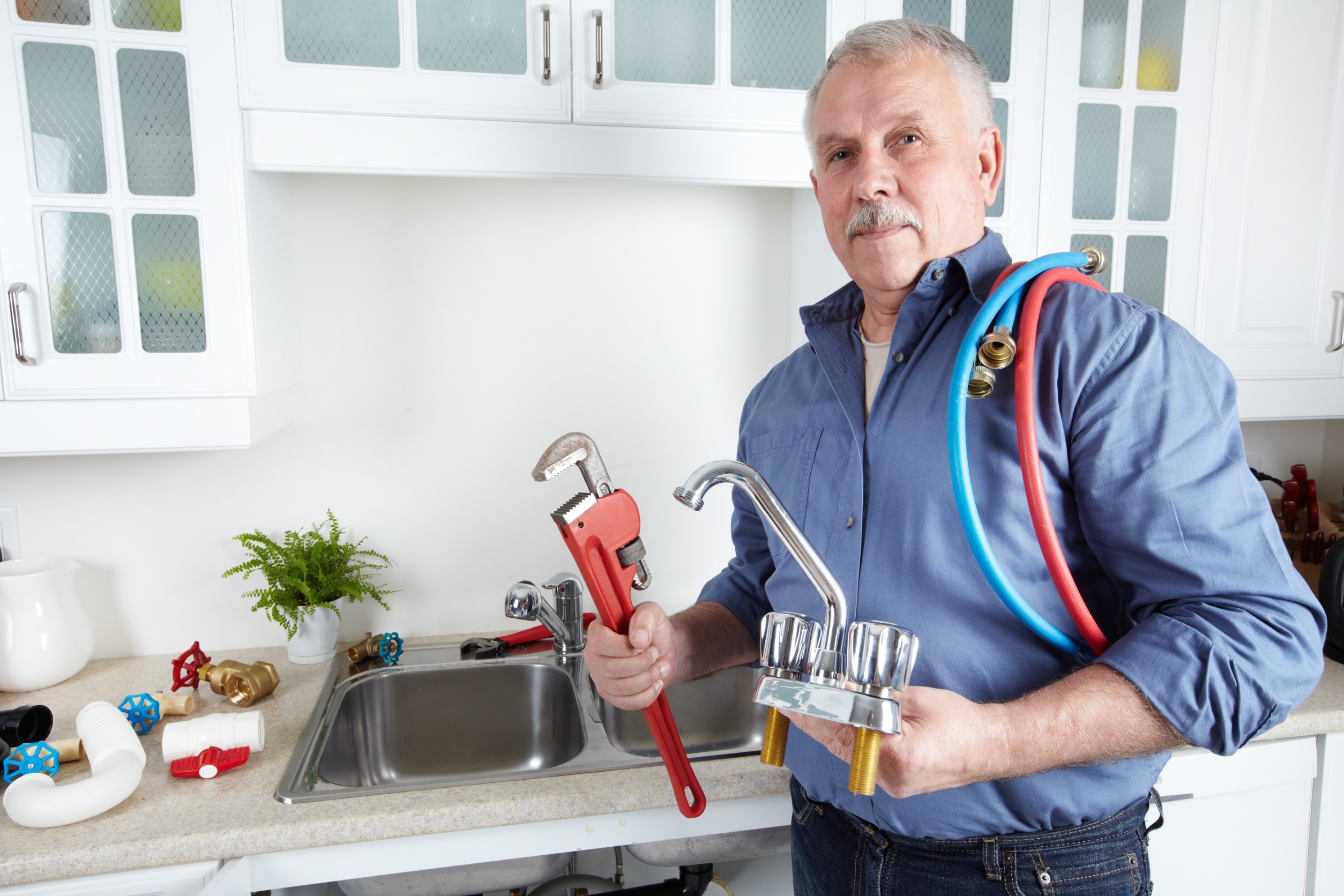 Plombier tenant outils et robinet dans une cuisine.
