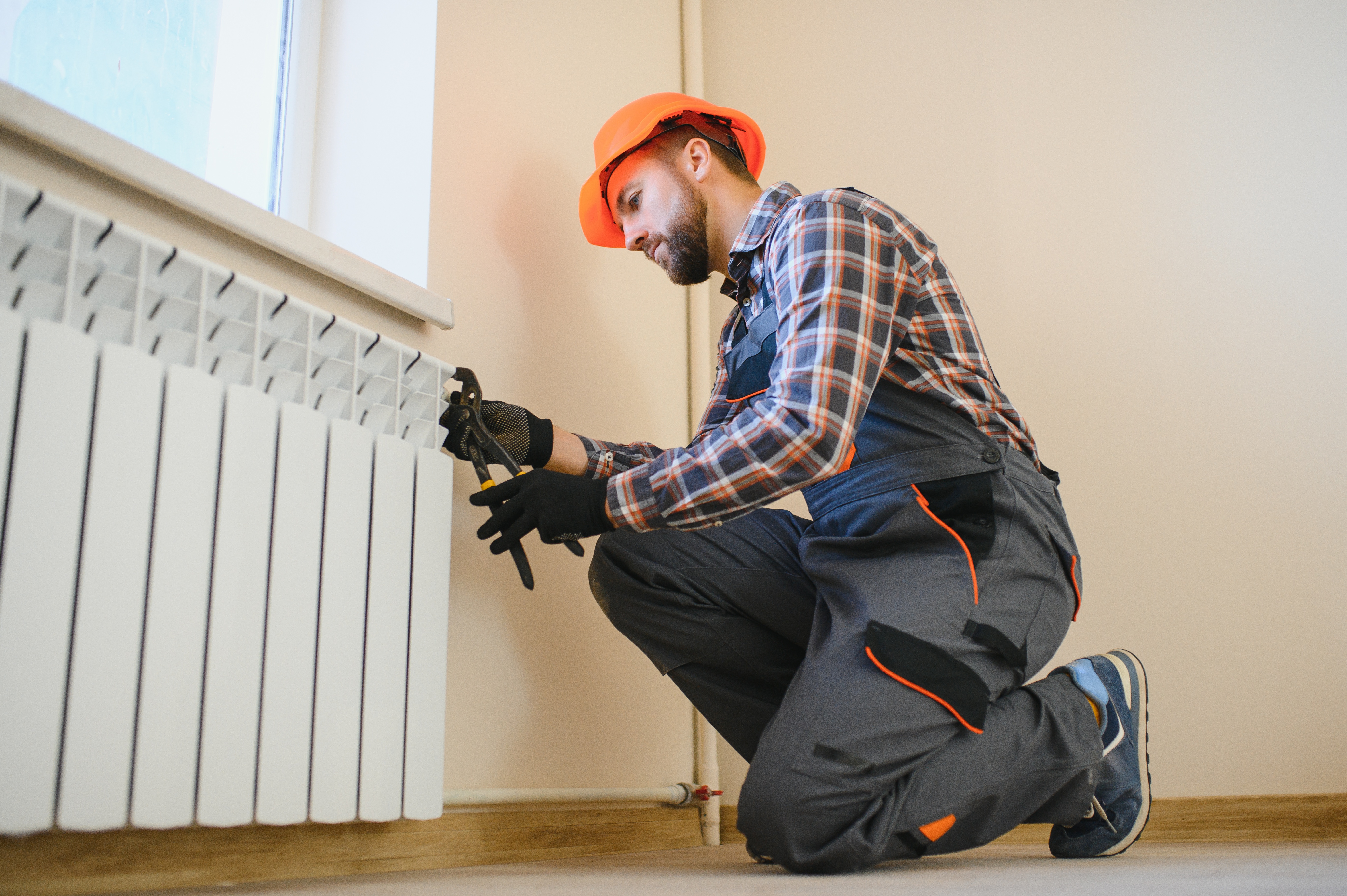 Technicien réparant un radiateur dans une pièce.